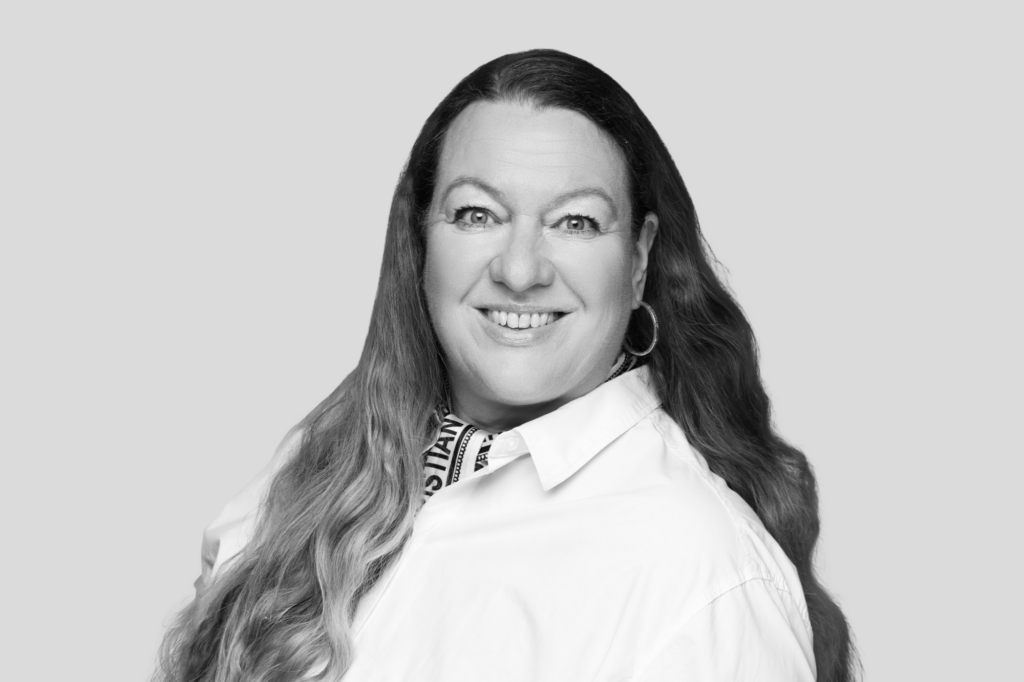 Porträt einer lächelnden Frau mit langen Haaren, weißem Hemd und gemustertem Halstuch.