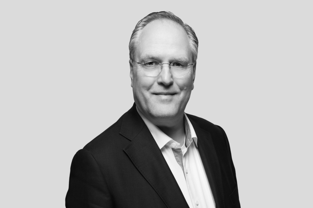 Porträt eines Mannes mit Brille und hellem Haar in Businesskleidung.