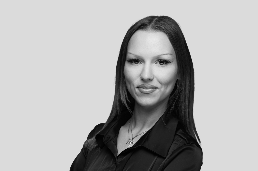 Porträt einer Frau mit glatten Haaren, Nasenpiercing und dunkler Bluse.