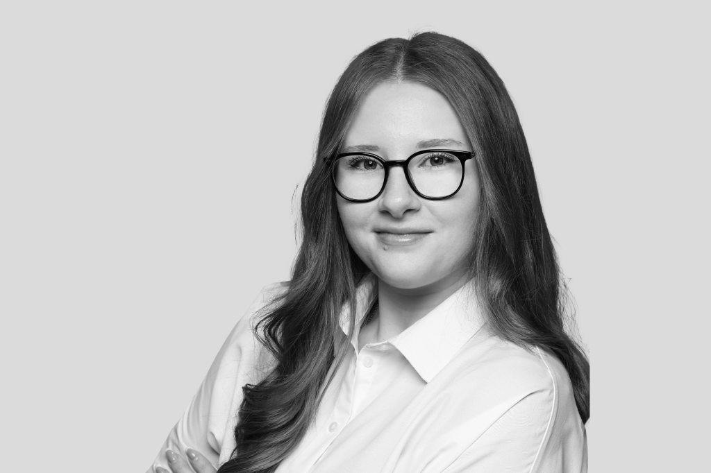 Porträt einer jungen Frau mit Brille und langen Haaren, trägt ein weißes Hemd.