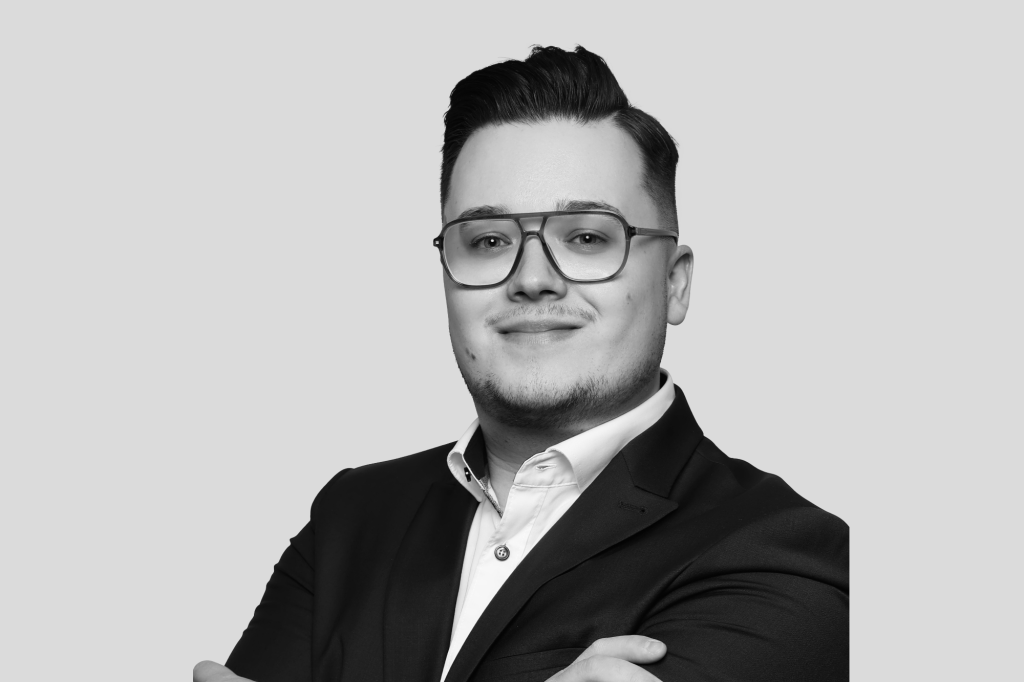 Porträt eines jungen Mannes mit Brille, Bartansatz und Anzugjacke.